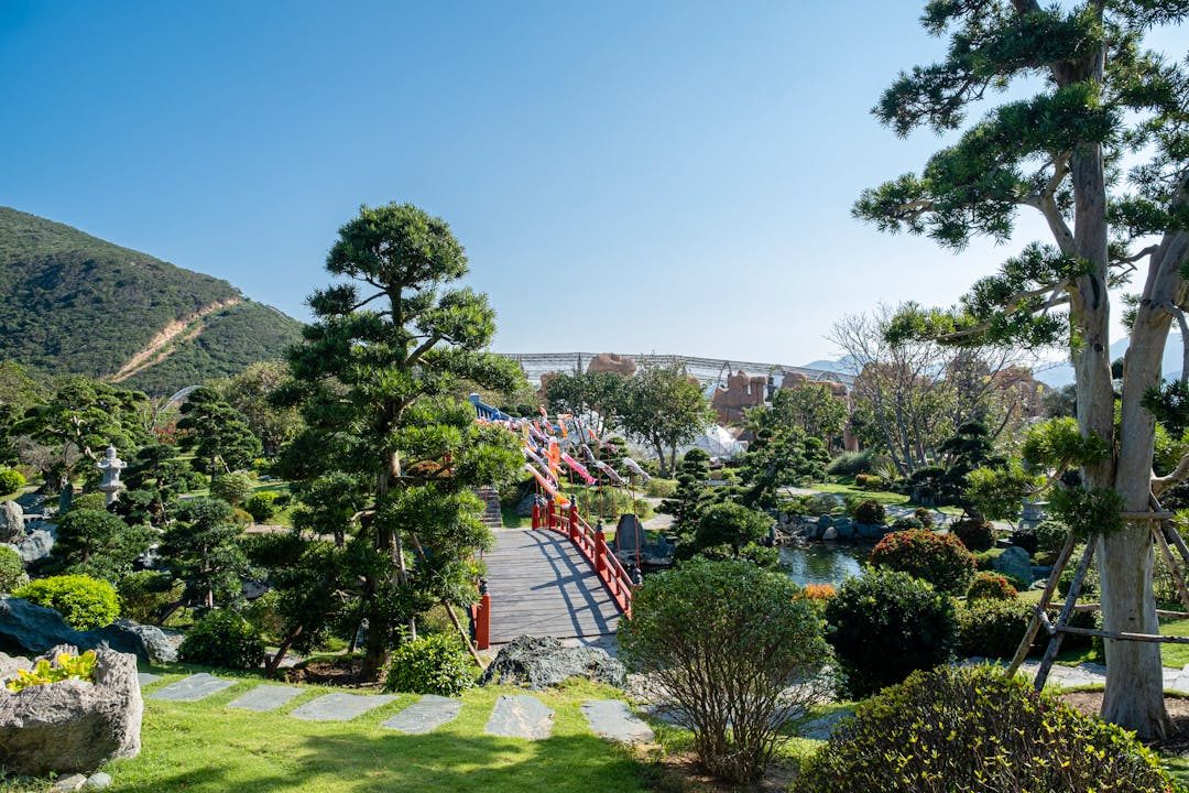 Scenic view of a lush Japanese garden featuring a traditional red bridge surrounded by greenery.