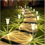 The image shows a garden stake light pack, illuminating a pathway in a beautiful outdoor setting.