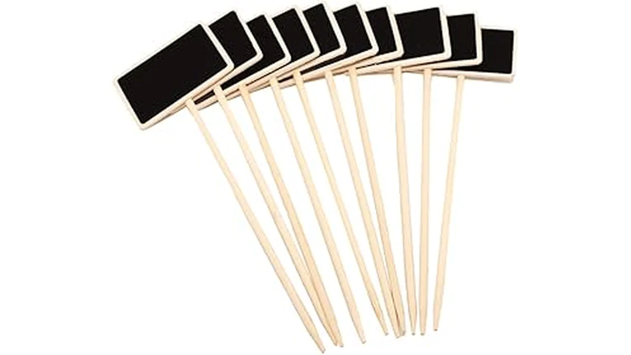 The image shows rustic chalkboard plant labels on stakes in a garden setting.